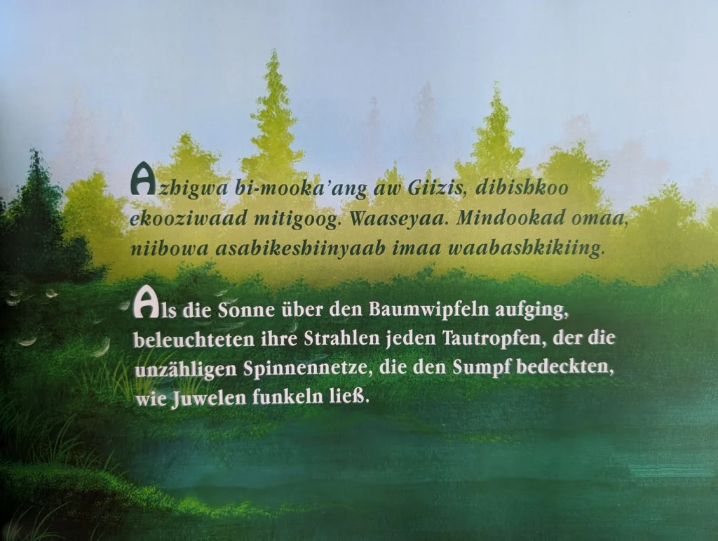 Innenseite mit einer Waldlandschaft und Text auf Ojibwe und Deutsch