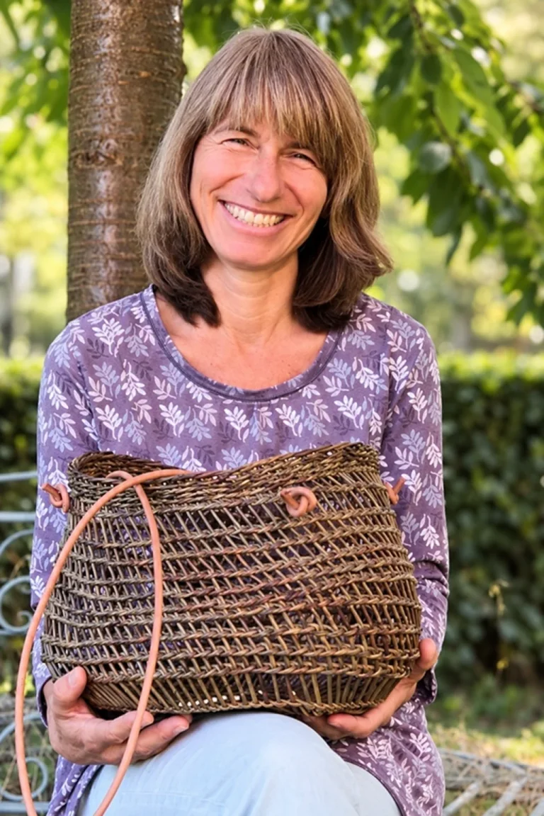 Regina Sommer lächelt im Grünen und hält einen selbst geflochtenen Korb.
